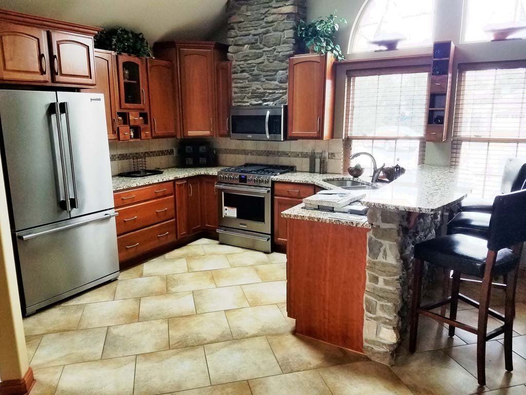 Kitchen with wood cabinets, stone accents, stainless steel appliances, granite countertops, and tile floor.