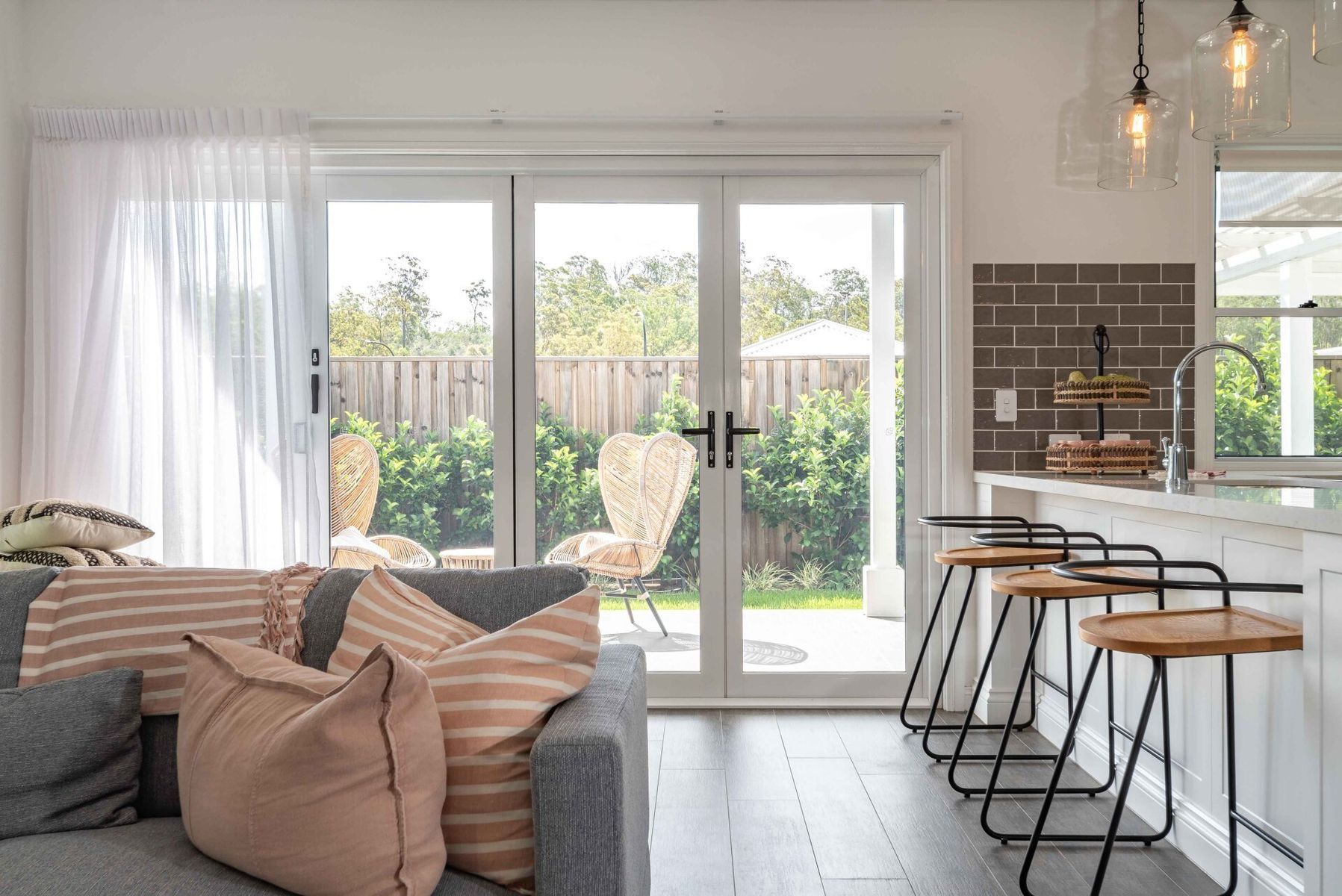 Living room with gray sofa, glass doors to the backyard, and a kitchen island with bar stools.