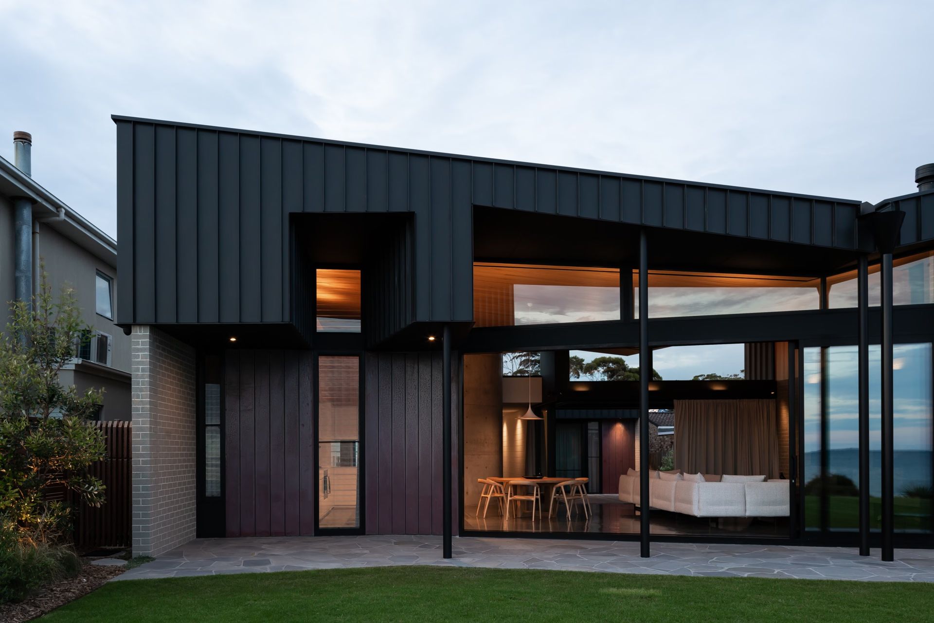 Modern home with dark exterior, large windows, and outdoor lawn.