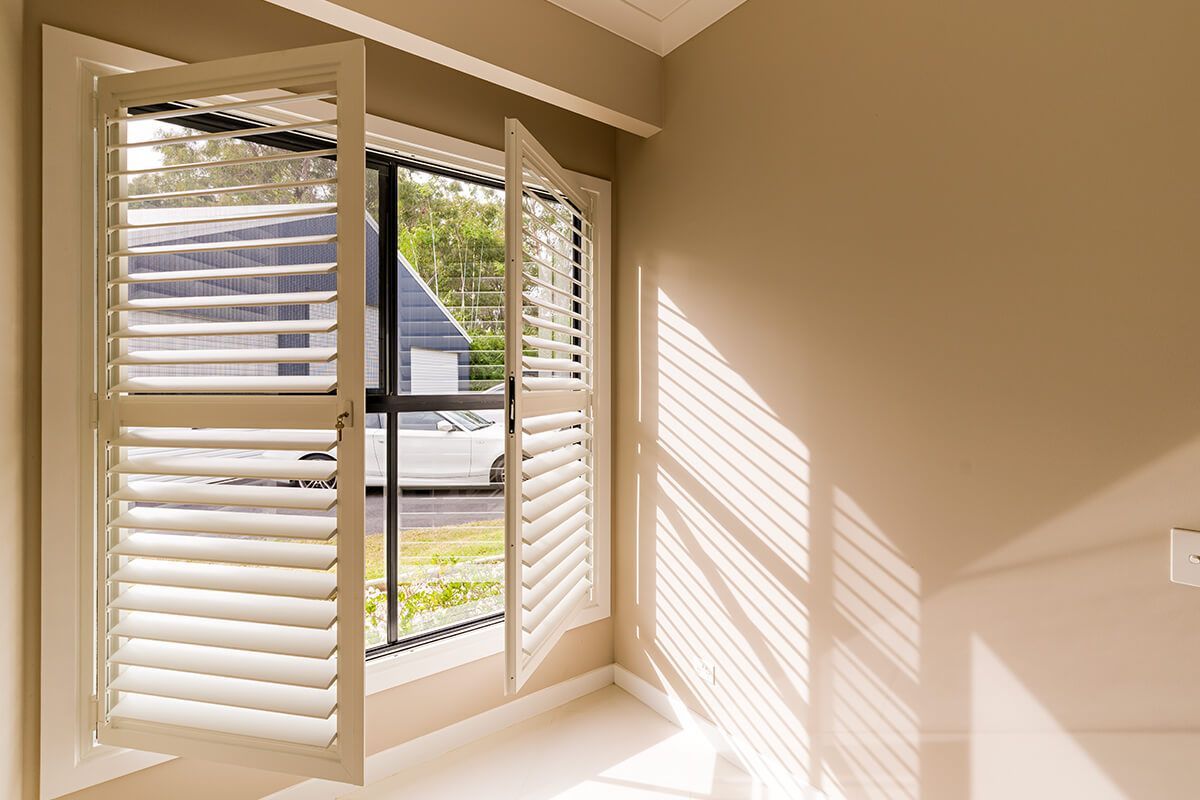 Open white window shutters with view of outside, casting shadows on tan walls.