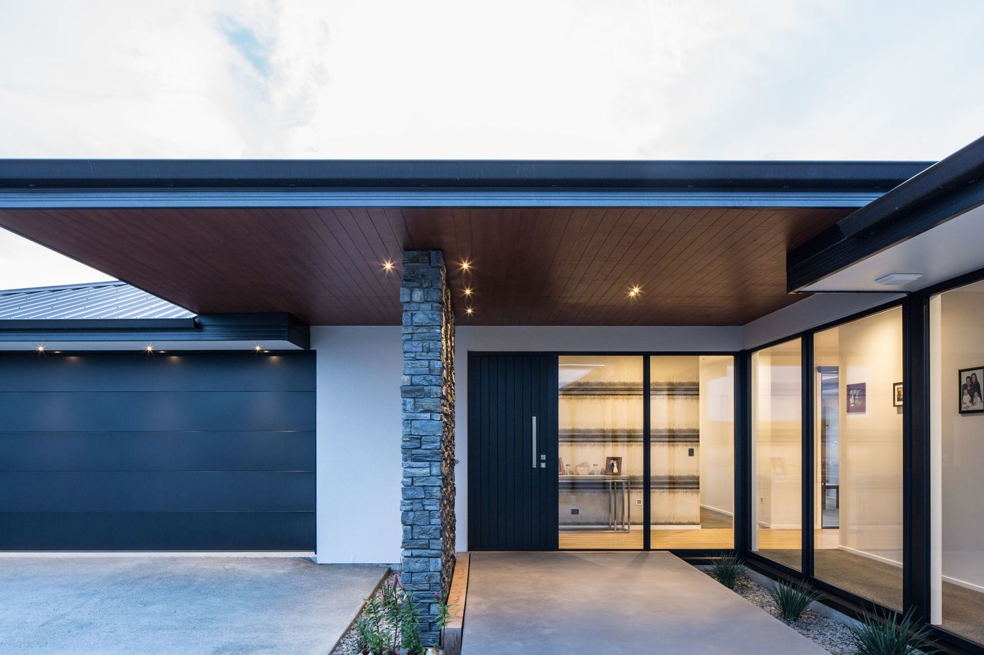 Modern kitchen with black glossy cabinets, white countertops, large window overlooking a yard.