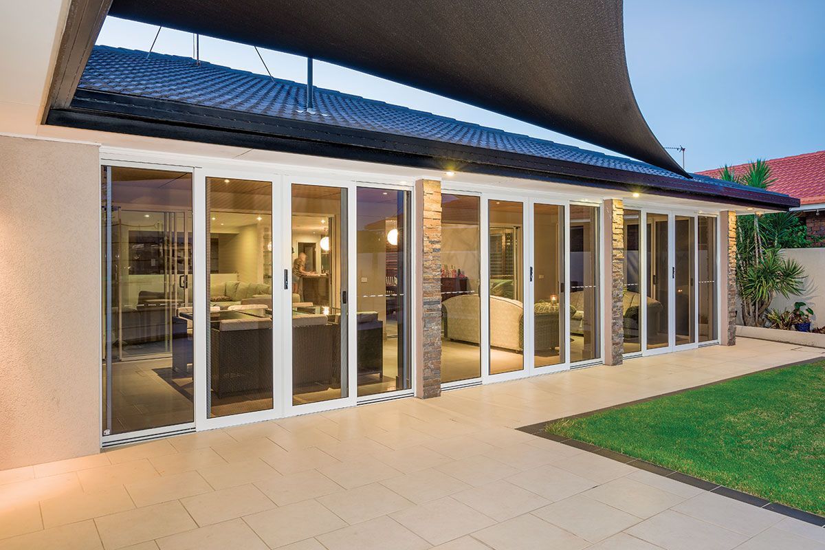 Open glass doors lead to an outdoor patio with green grass and a shade sail.