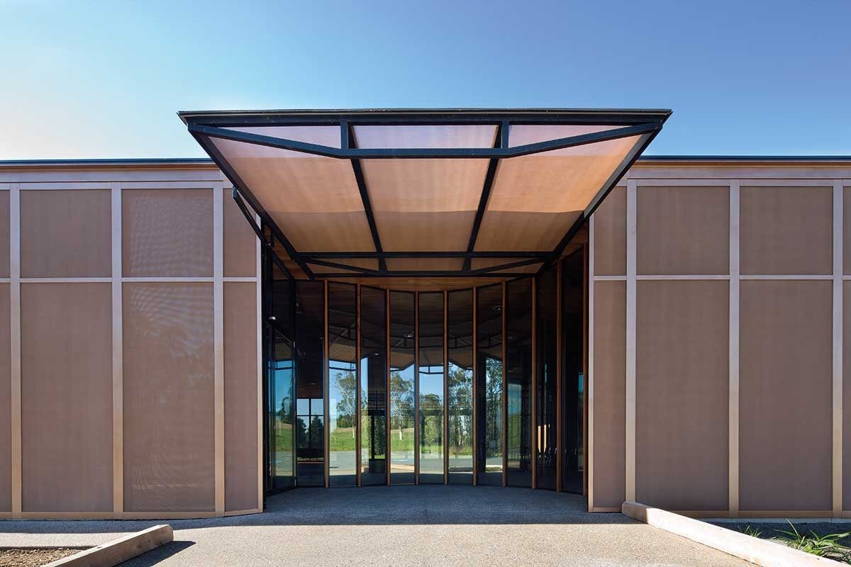 Modern building entrance with brown mesh walls, glass doors, and a black metal awning.