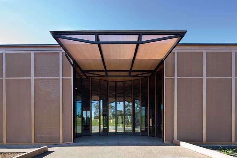 Building entrance with metal frame awning over glass doors and mesh side panels.