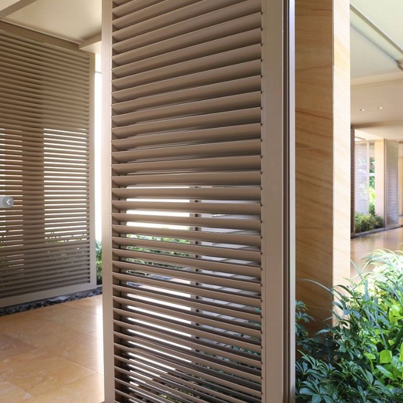 Beige rolling shutter on a window of a light-colored house, next to a porch with columns and a dining area.