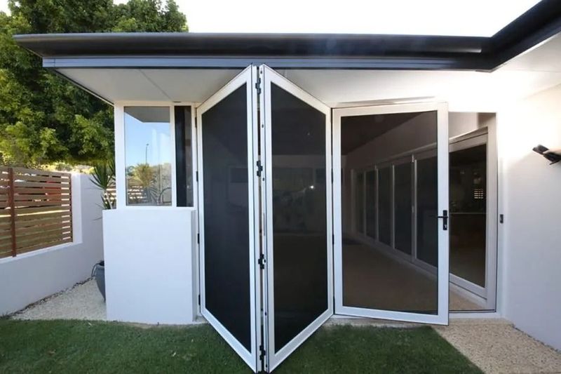 White folding doors with black screens, beside a window. Outdoors, next to a building.