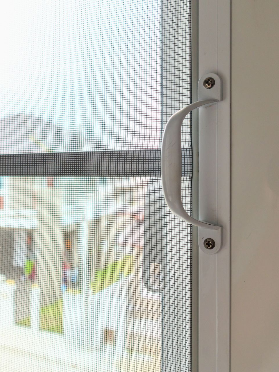 Close-up of white screen door with handle. Mesh screen allows view of blurred outdoor scene.