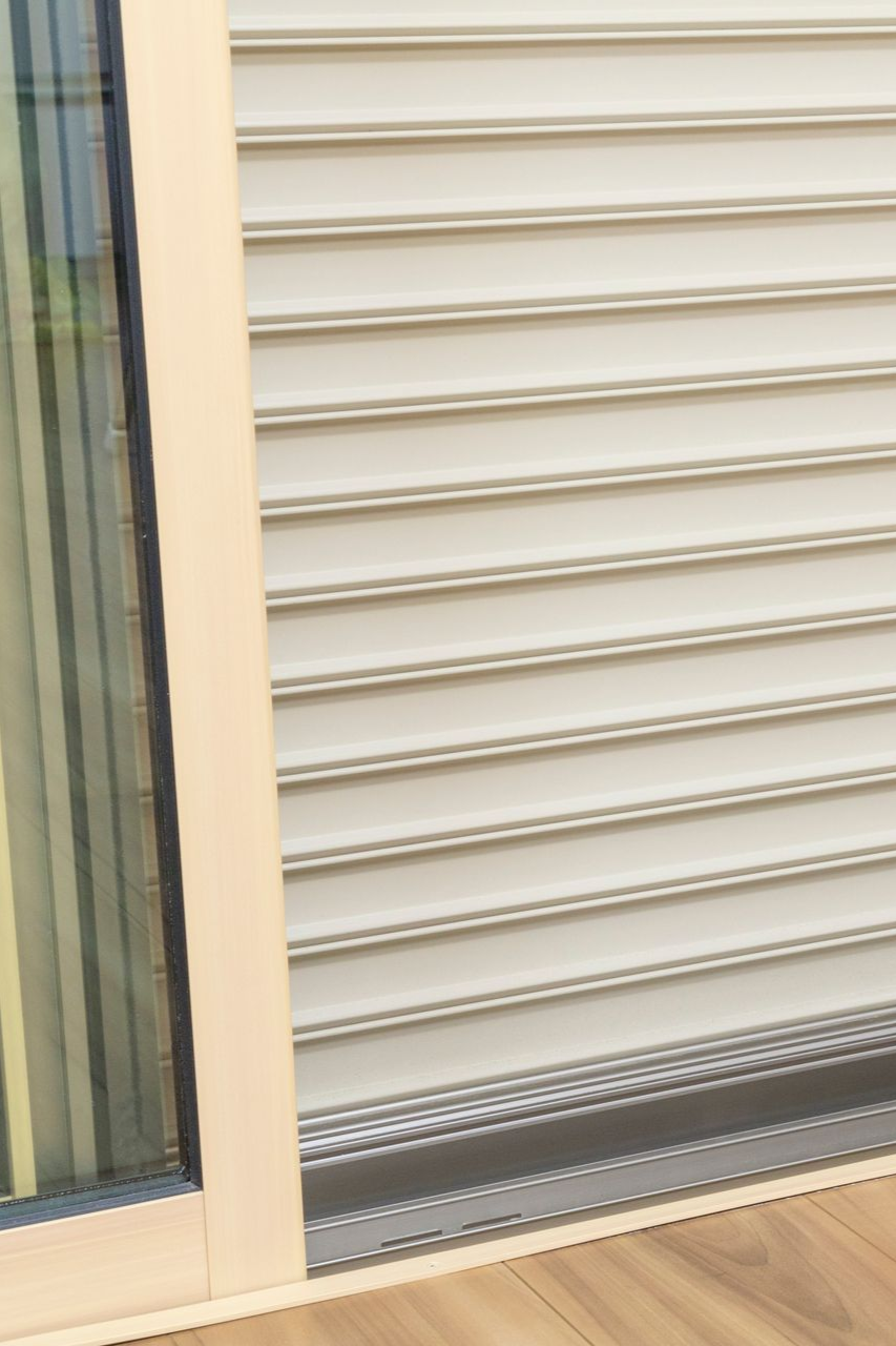Beige horizontal roll-up shutter covering a window, viewed from the side.