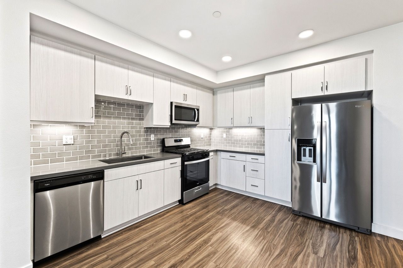 Modern apartment kitchen with stainless steel appliances, white cabinets, and gray subway tile backsplash.