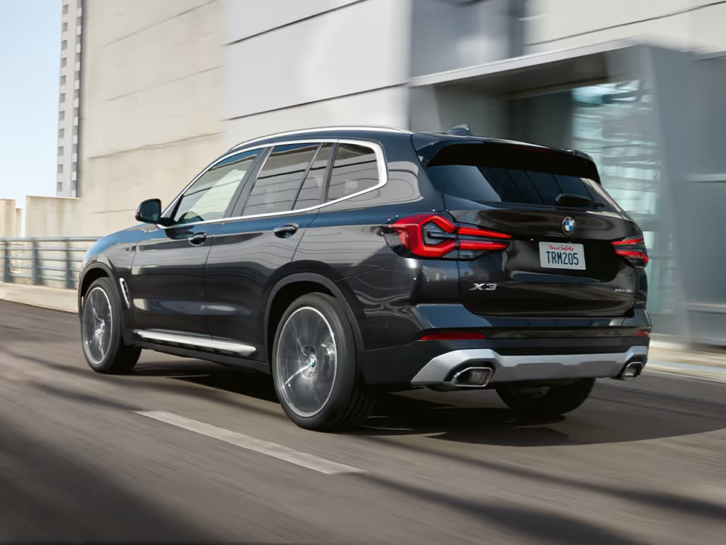 Black BMW X3 SUV driving on a road next to a building.