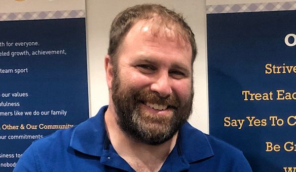 Man with a beard smiling in front of a blue background with text.