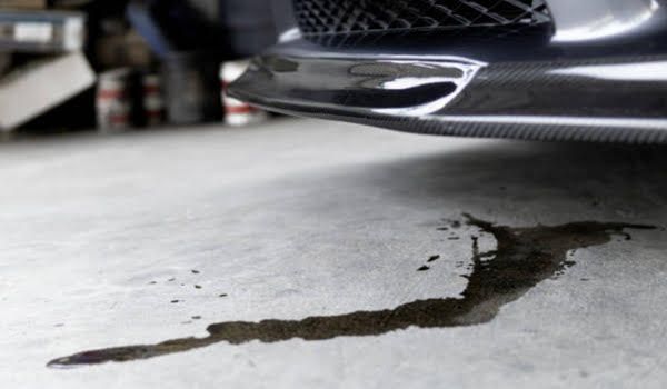 Black car leaking fluid on a concrete floor.