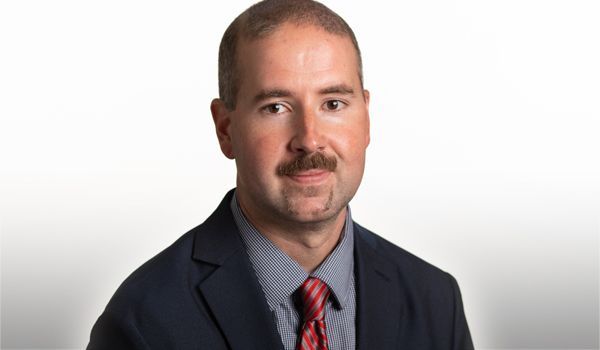 Man in a suit and tie, smiling, against a white background.