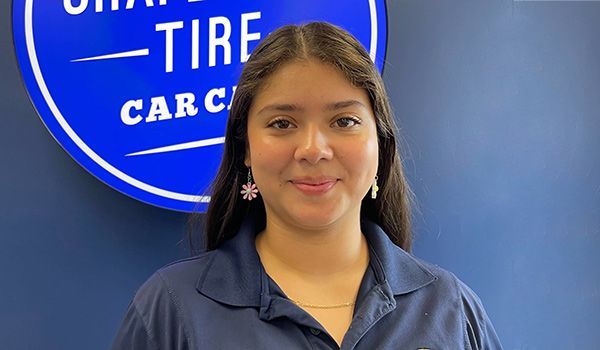 Woman in blue shirt smiles in front of a blue and white sign for a tire shop.