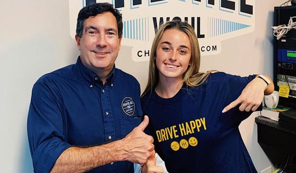 A man and a woman are posing for a picture . the woman is wearing a shirt that says drive happy.