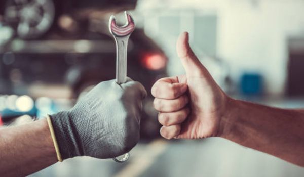 A mechanic is giving a thumbs up while holding a wrench.