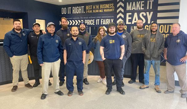 A group of people standing in front of a blue wall with text. Most are wearing work attire.