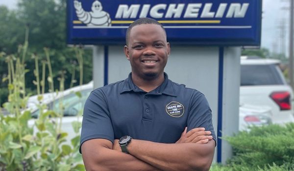 A man is standing in front of a michelin sign with his arms crossed.