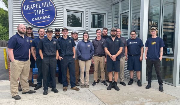 Group of people, possibly employees, in front of Chapel Hill Tire. People wearing blue shirts and khaki pants.