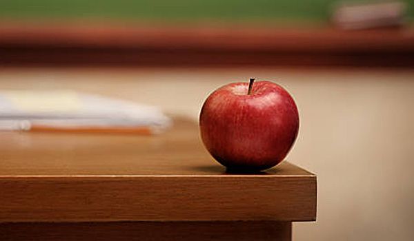 Red apple on a wooden desk in a classroom.