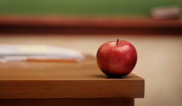 Red apple on a wooden desk. In the background, there's a blurred green and brown wall.
