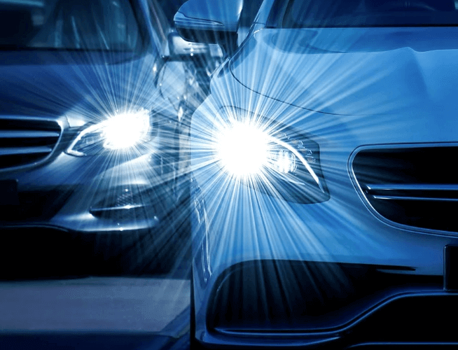 Two cars are parked next to each other and their headlights are shining brightly