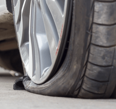 Flat car tire on a concrete surface. The tire is deflated and damaged.