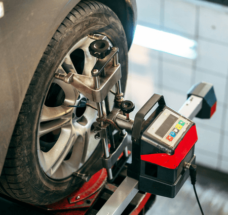 Car tire undergoing alignment check with attached equipment in a garage.