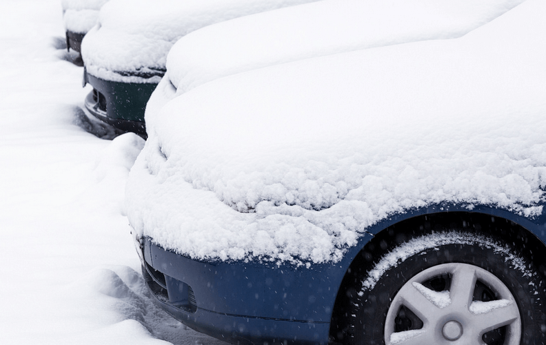 A row of cars covered in snow in a parking lot