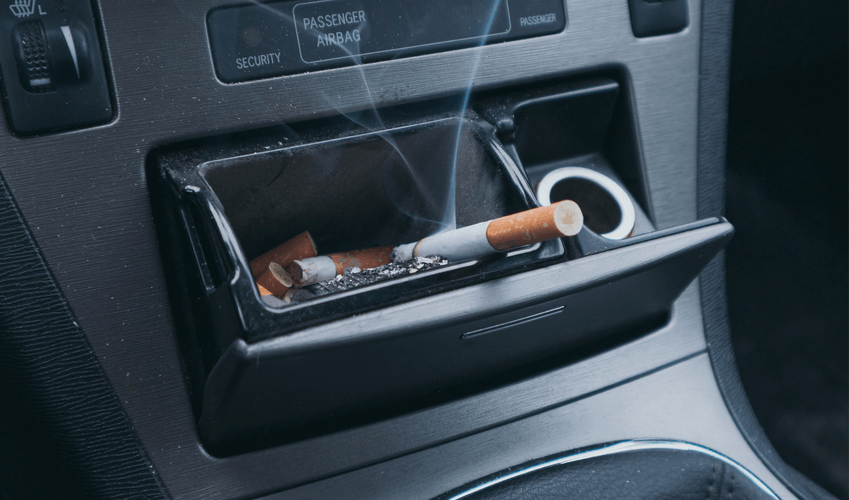 Ashtray in car with lit and spent cigarettes, smoke rising.