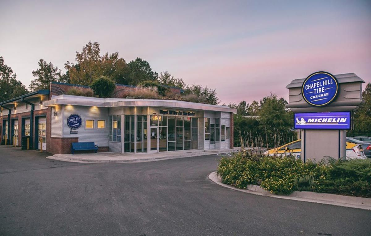 Exterior of a tire shop with a green roof, blue accents, and a Michelin sign. Dusk sky.