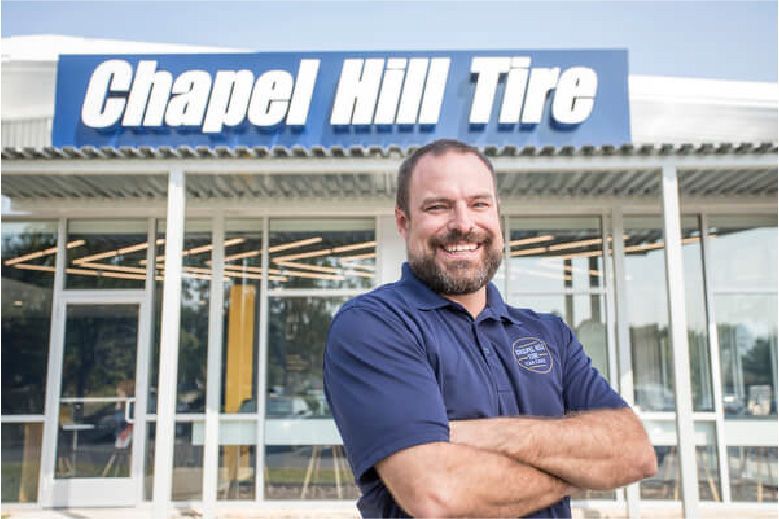 Man in blue shirt smiles in front of Chapel Hill Tire shop.