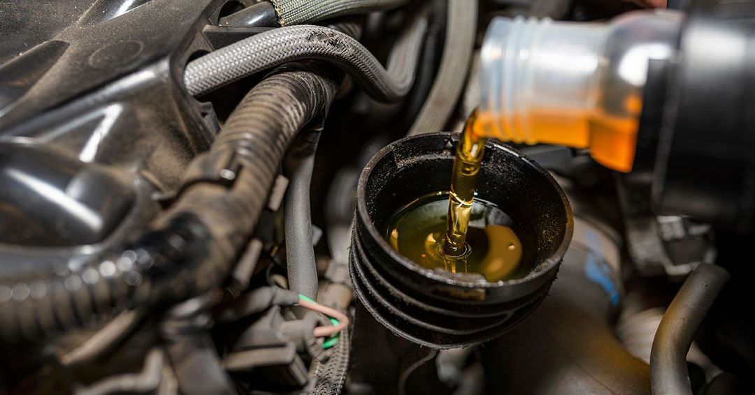 Engine oil being poured into a car's oil filler tube; black engine parts visible.