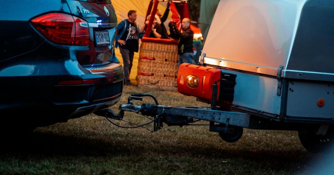 A car is towing a trailer with a hot air balloon in the background