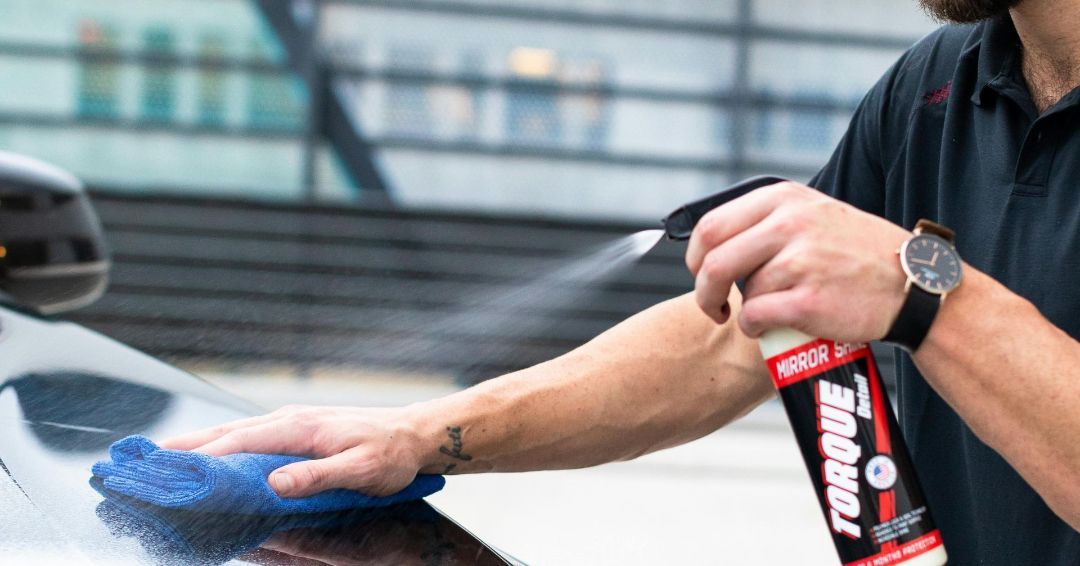 Man spraying car with a spray bottle and wiping with a blue cloth.