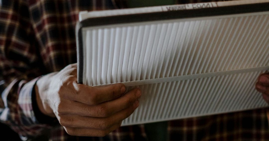 Person holding a rectangular air filter with white, ridged surface.