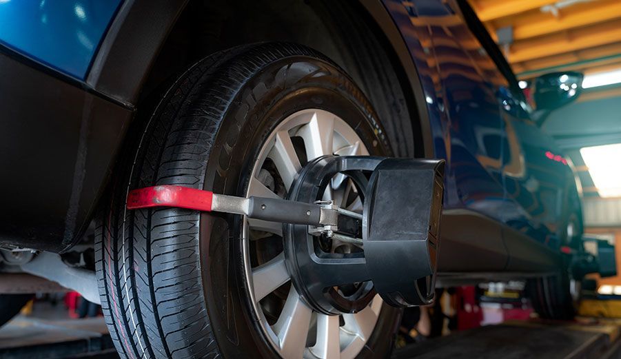 Tire alignment being performed on a blue car in a repair shop. A black alignment tool is attached to the tire.