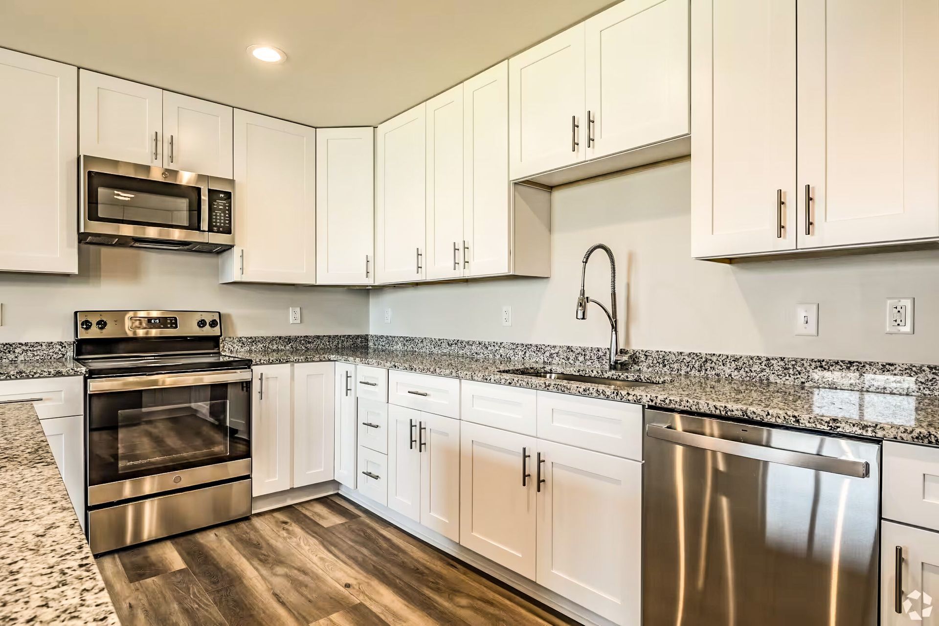 Modern white kitchen with stainless steel appliances, granite countertops, and wood-look flooring