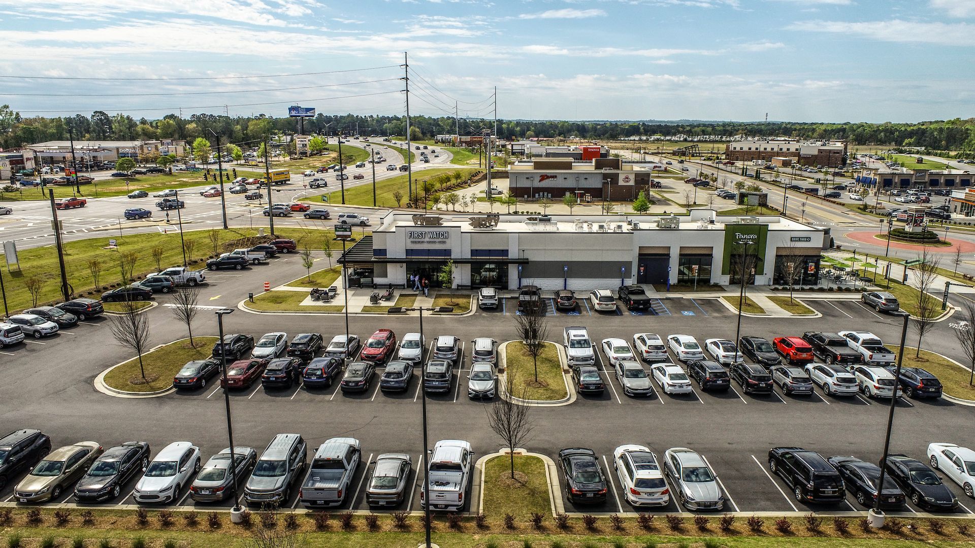Aerial view of a busy shopping center with rows of parked cars and surrounding roads.