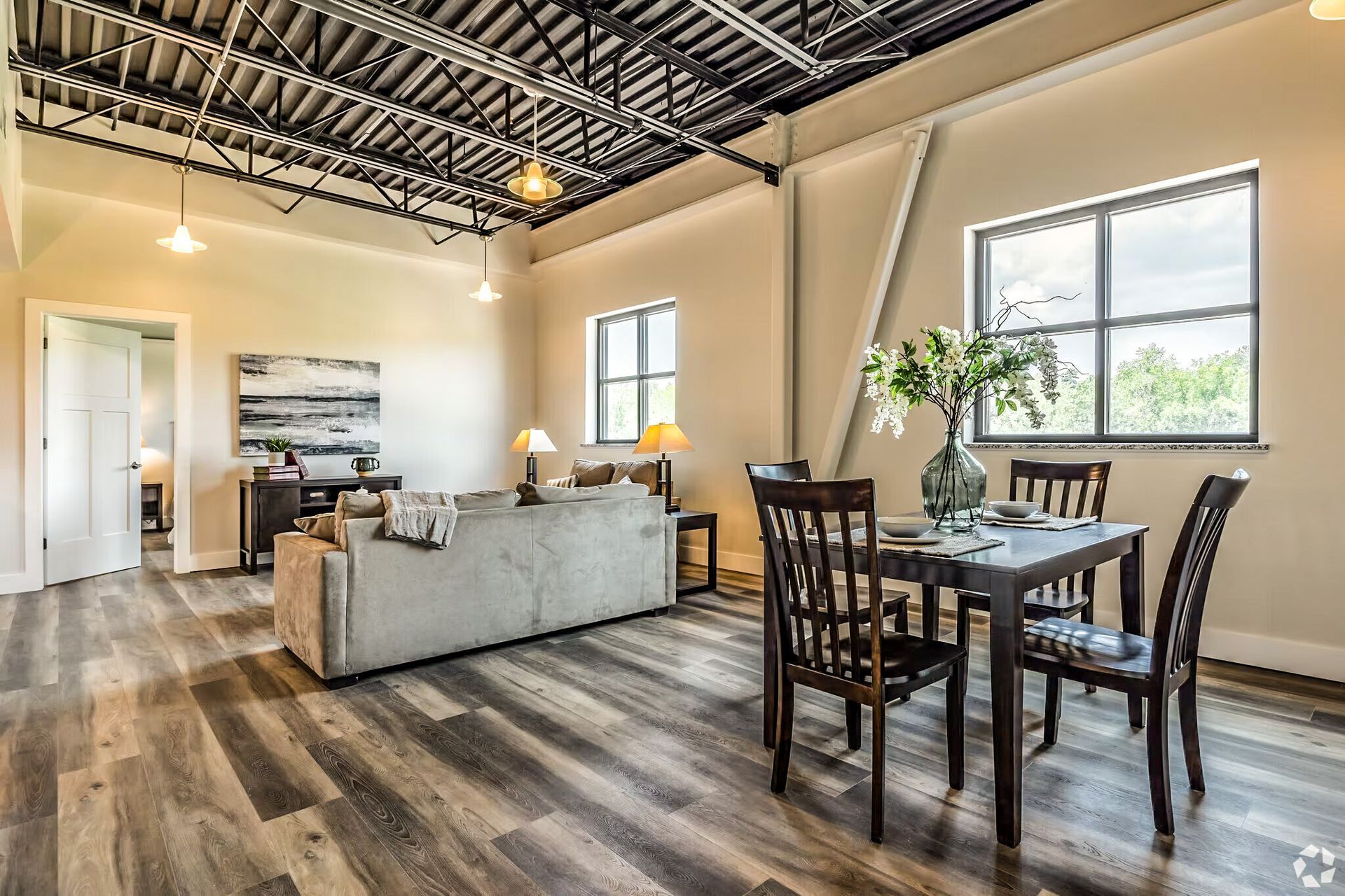 Open-plan living and dining room with high ceilings, gray sofa, wood table, and large windows