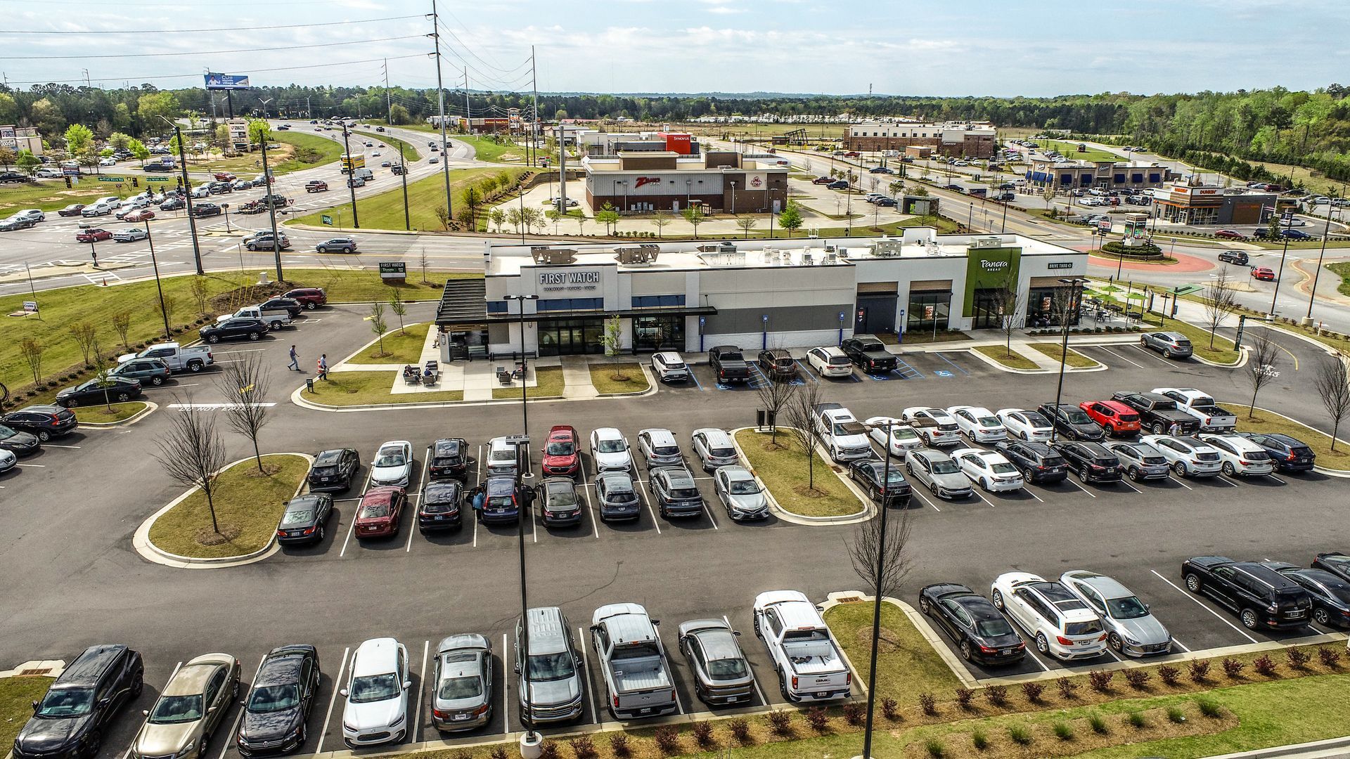 Aerial view of a busy shopping center parking lot with many cars and stores in the background