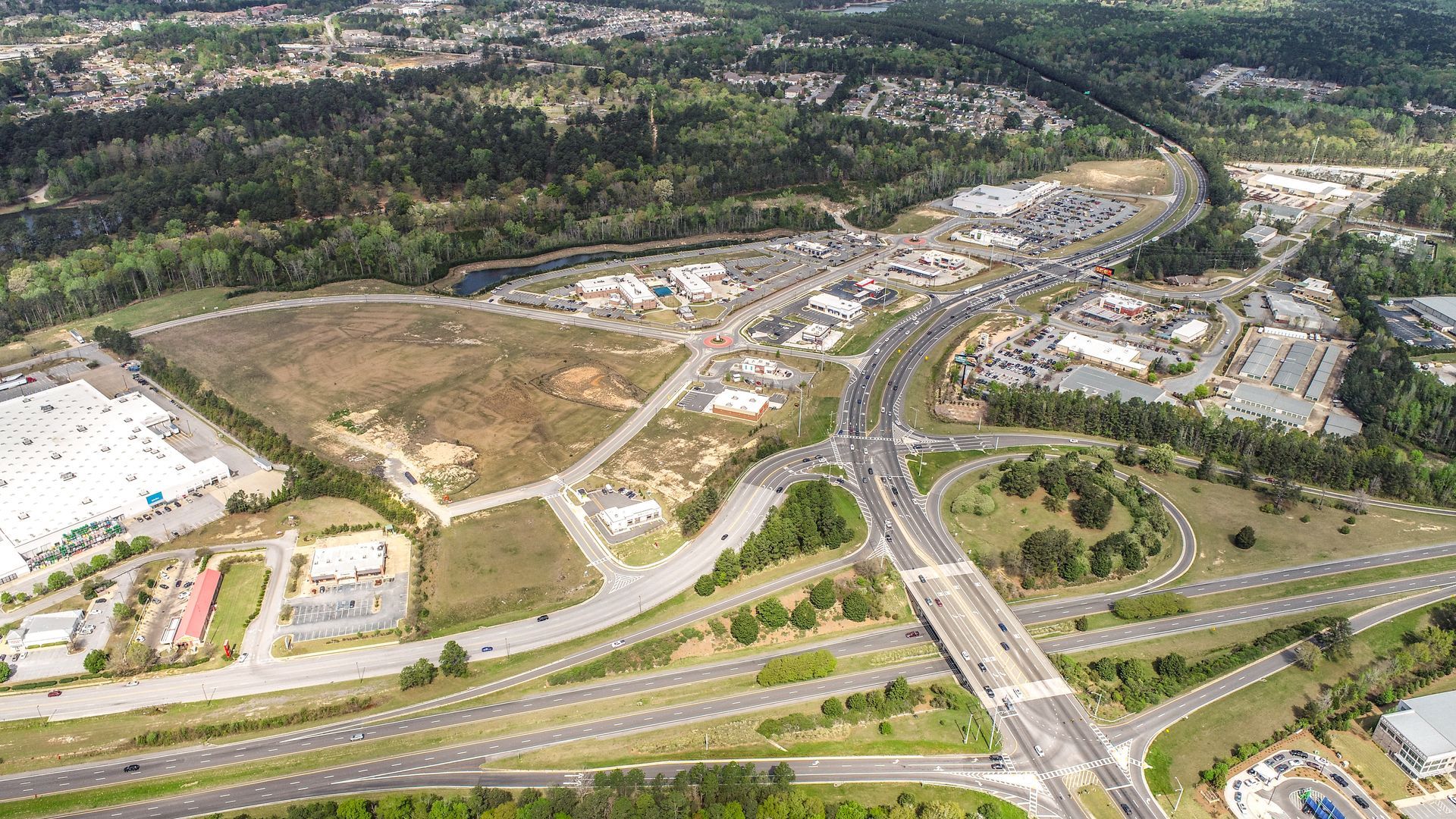 Aerial view of a large highway interchange beside a brown construction site and suburban buildings.