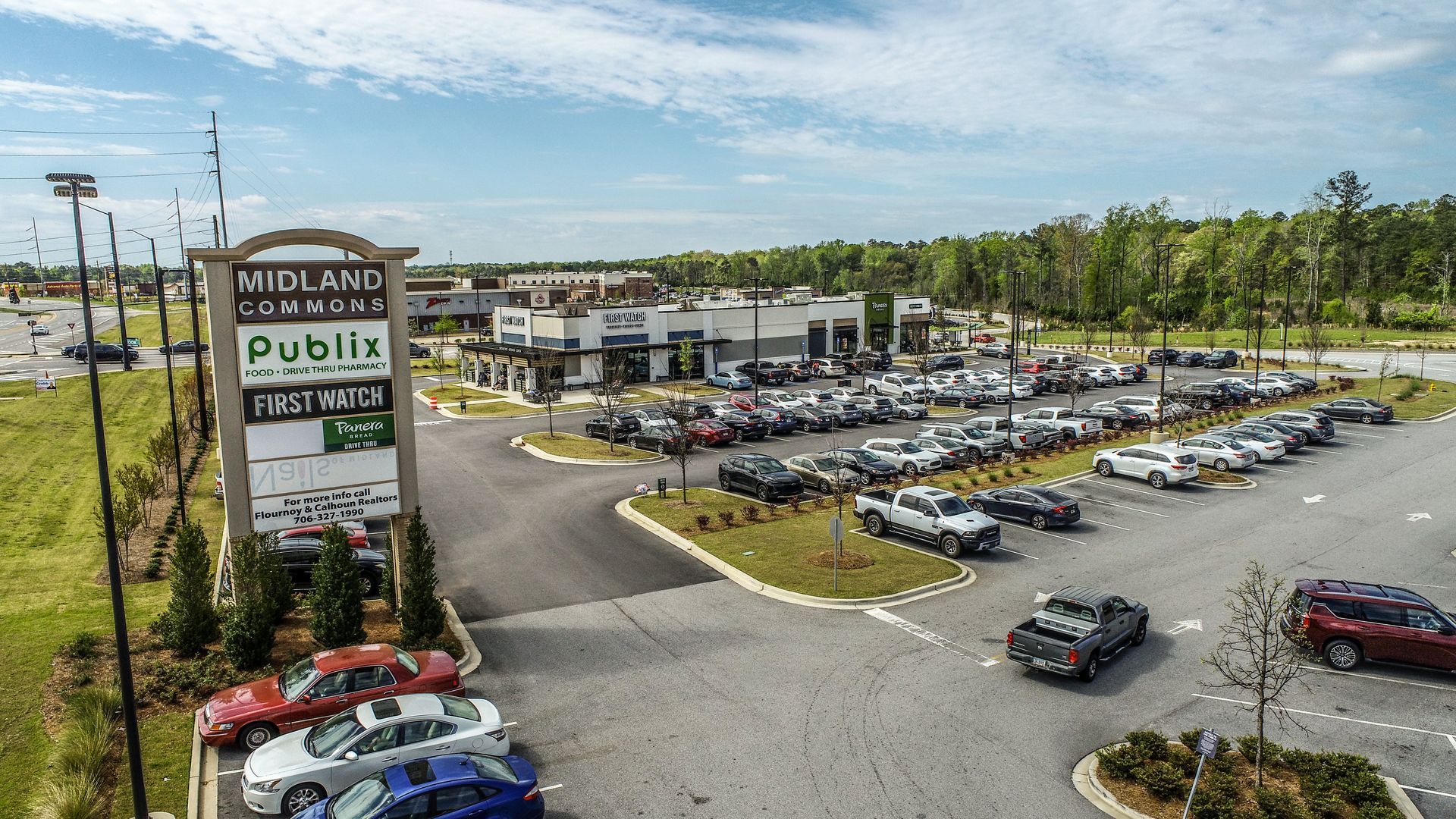 Car dealership lot with rows of cars and a large “Public” roadside sign on a sunny day