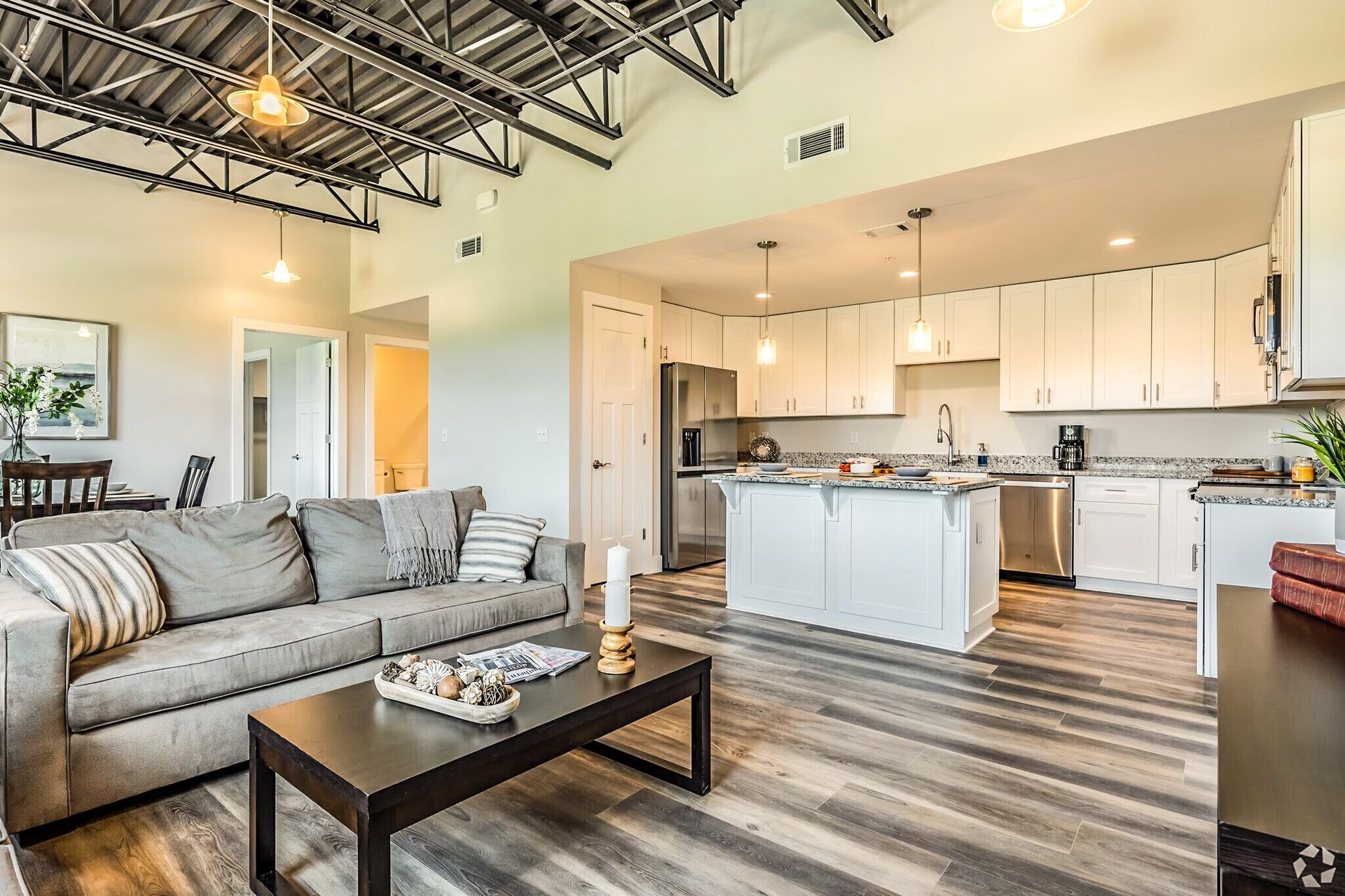 Modern open-concept living room with gray sofa, coffee table, and white kitchen with island and pendant lights