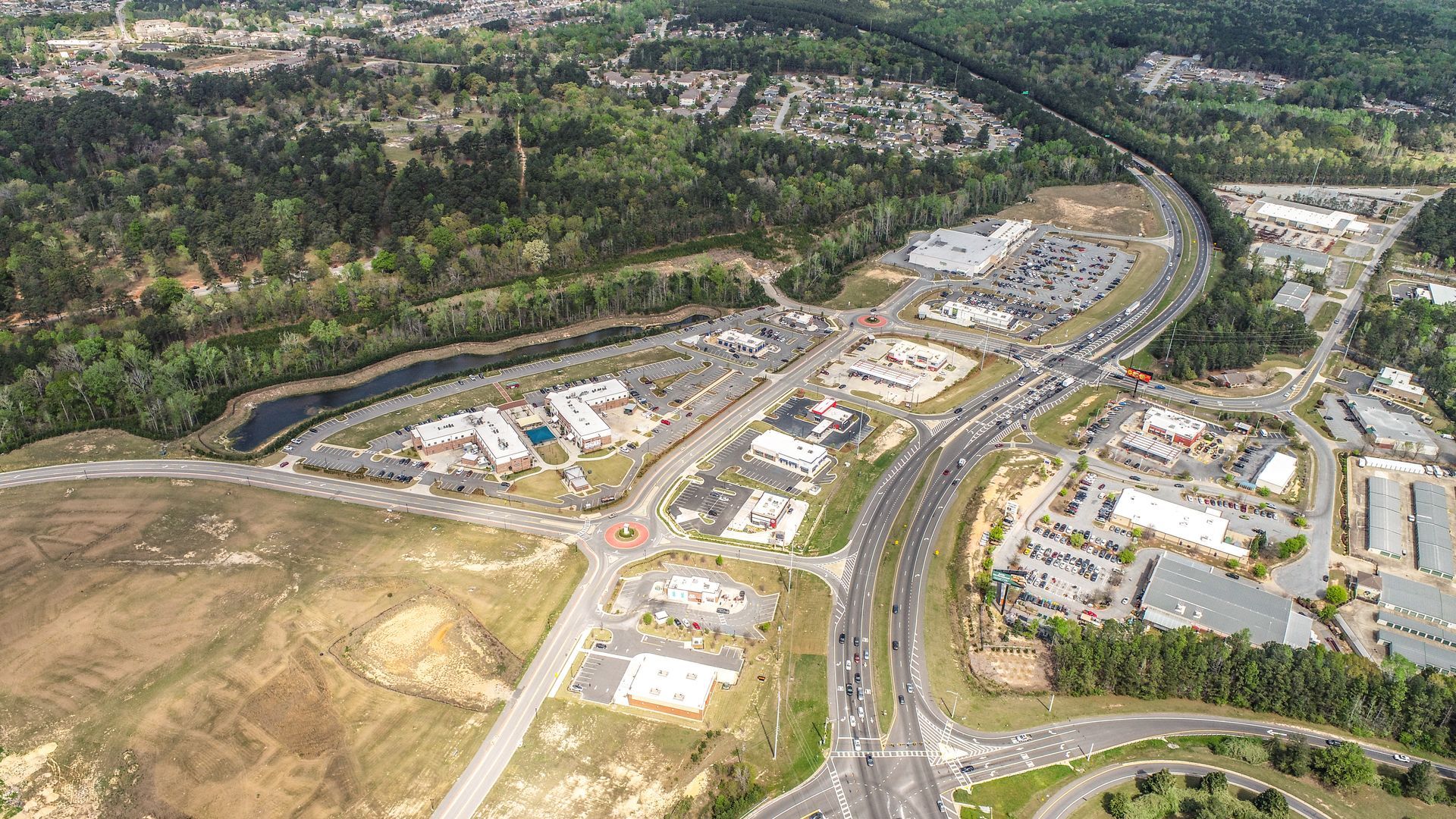 Aerial view of a new suburban development with roads, houses, and cleared construction lots beside wooded hills