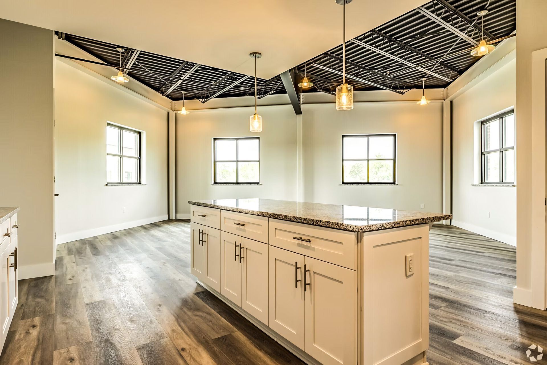 Bright kitchen with a large island, white cabinets, wood floors, and black ceiling beams.
