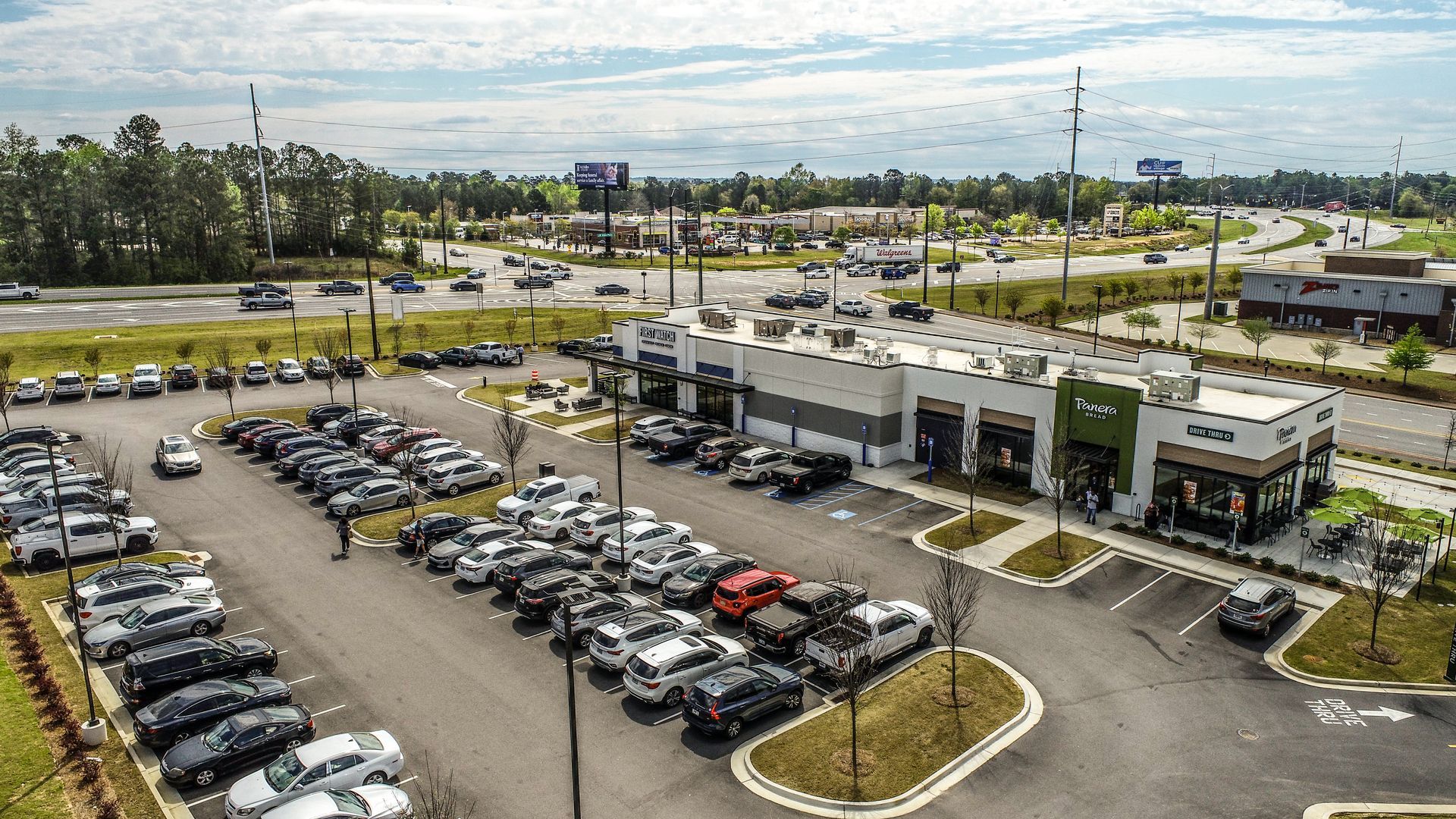 Aerial view of a car dealership lot with rows of parked vehicles and a showroom building.