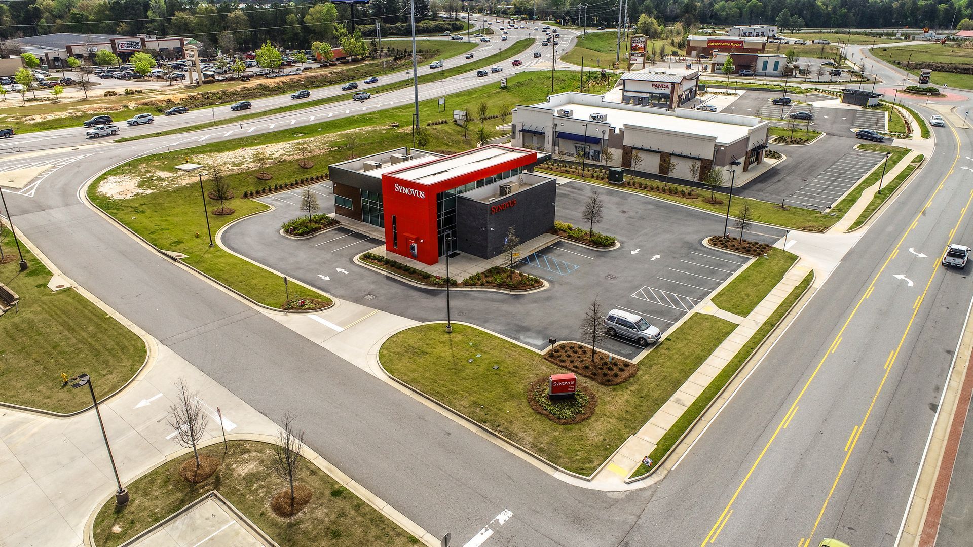 Aerial view of a red commercial building with parking lot at a road intersection in a suburban area
