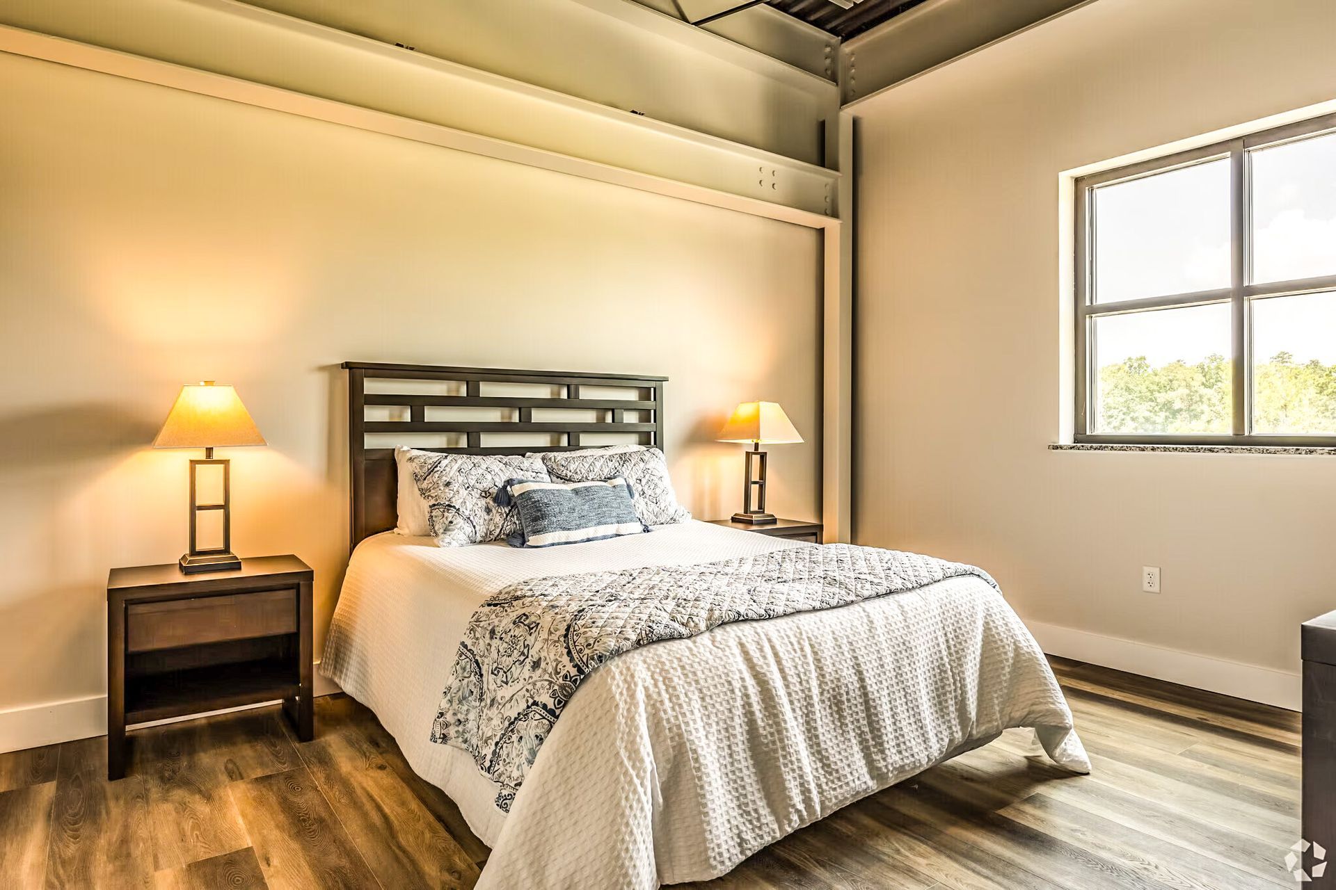 Cozy bedroom with a bed, nightstands, warm lamps, and a large window