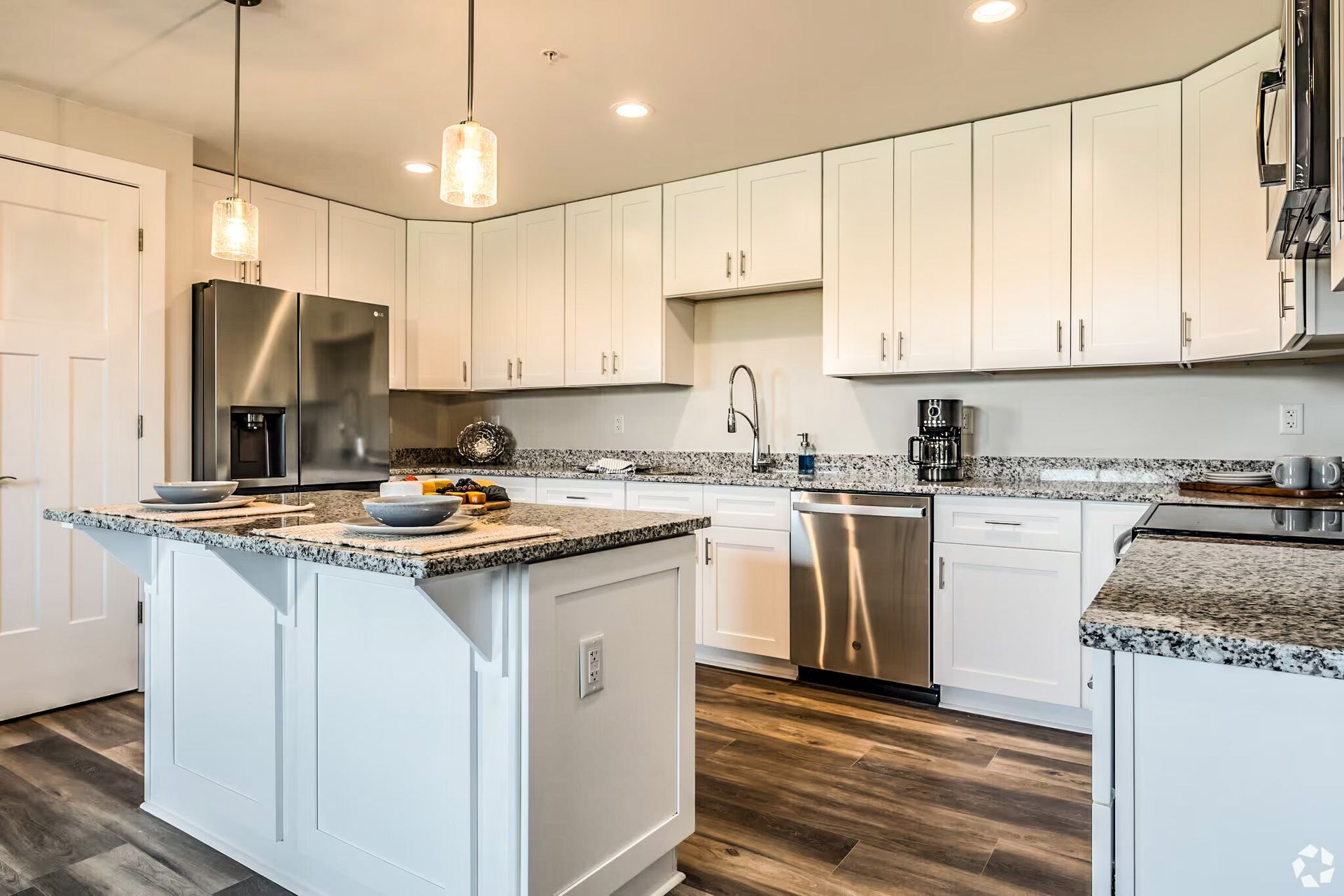 Bright modern kitchen with white cabinets, marble island, stainless steel appliances, and wood floors